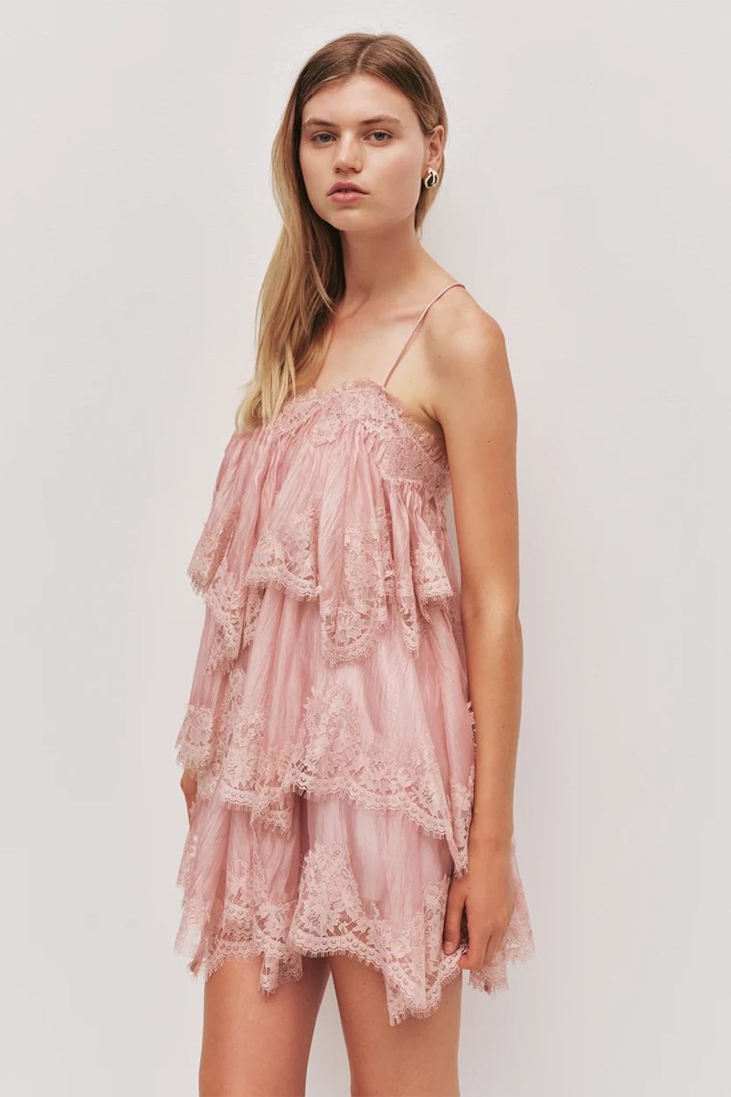 A model wears an Aje Ophelia Lace Mini Dress in fawn pink, a sleeveless style featuring tiered layers of lace trim.