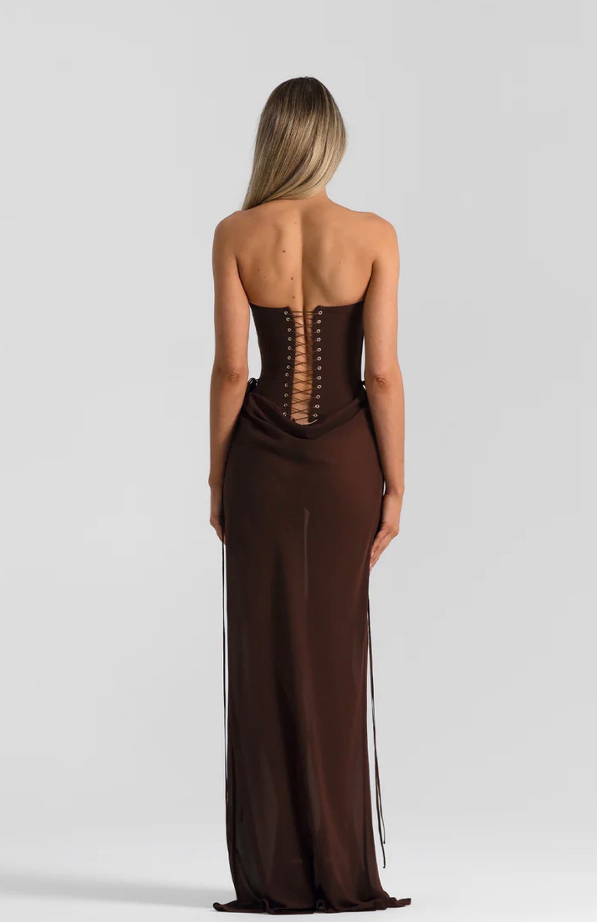 Back view of a person wearing a dark brown Natalie Rolt Verity & Allira Set featuring a strapless bustier and skirt with a corset-style lace-up back closure.