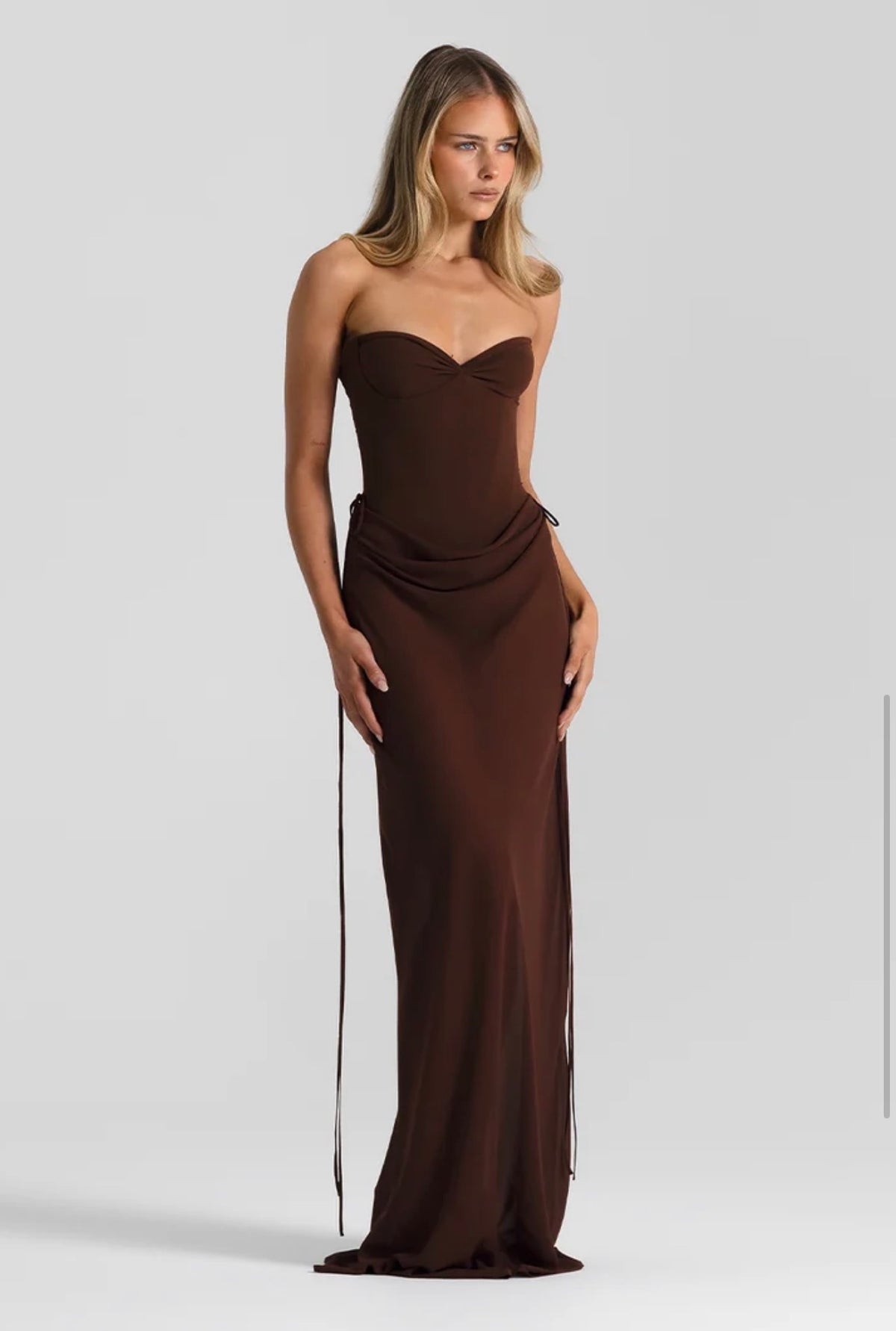 A person wearing the Verity & Allira Set, a chocolate-colored, strapless, floor-length gown with a sweetheart neckline, a bustier top, a matching skirt, and side ties.