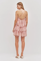 The Aje Ophelia Lace Mini Dress is a fawn pink lace dress with a tiered ruffled skirt and thin cross-back straps.