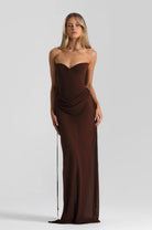 A woman wears the chocolate Verity & Allira Set, featuring a floor-length dark brown gown with a sweetheart neckline and a draped detail at the waist.