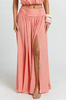 A coral-colored Melanie Set featuring a halter-neck crop top and a high-waisted maxi skirt with a side slit.