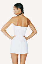 A woman with braided hair and jewelry stands with hands on hips, modeling the Chloe Corset Dress by With Jean—a strapless, form-fitting piece—shown from the back against a plain light background.