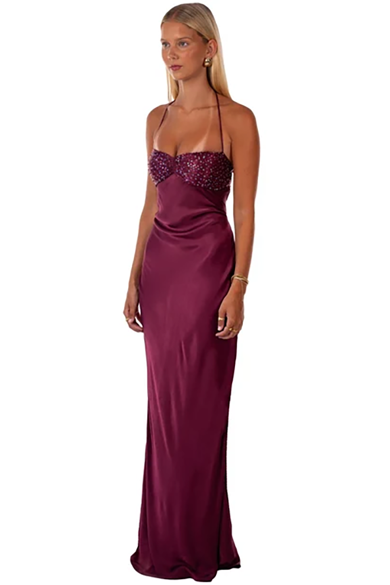 A person wears a berry-colored Jade Maxi Dress in Berry featuring a beaded bodice and thin halter straps.